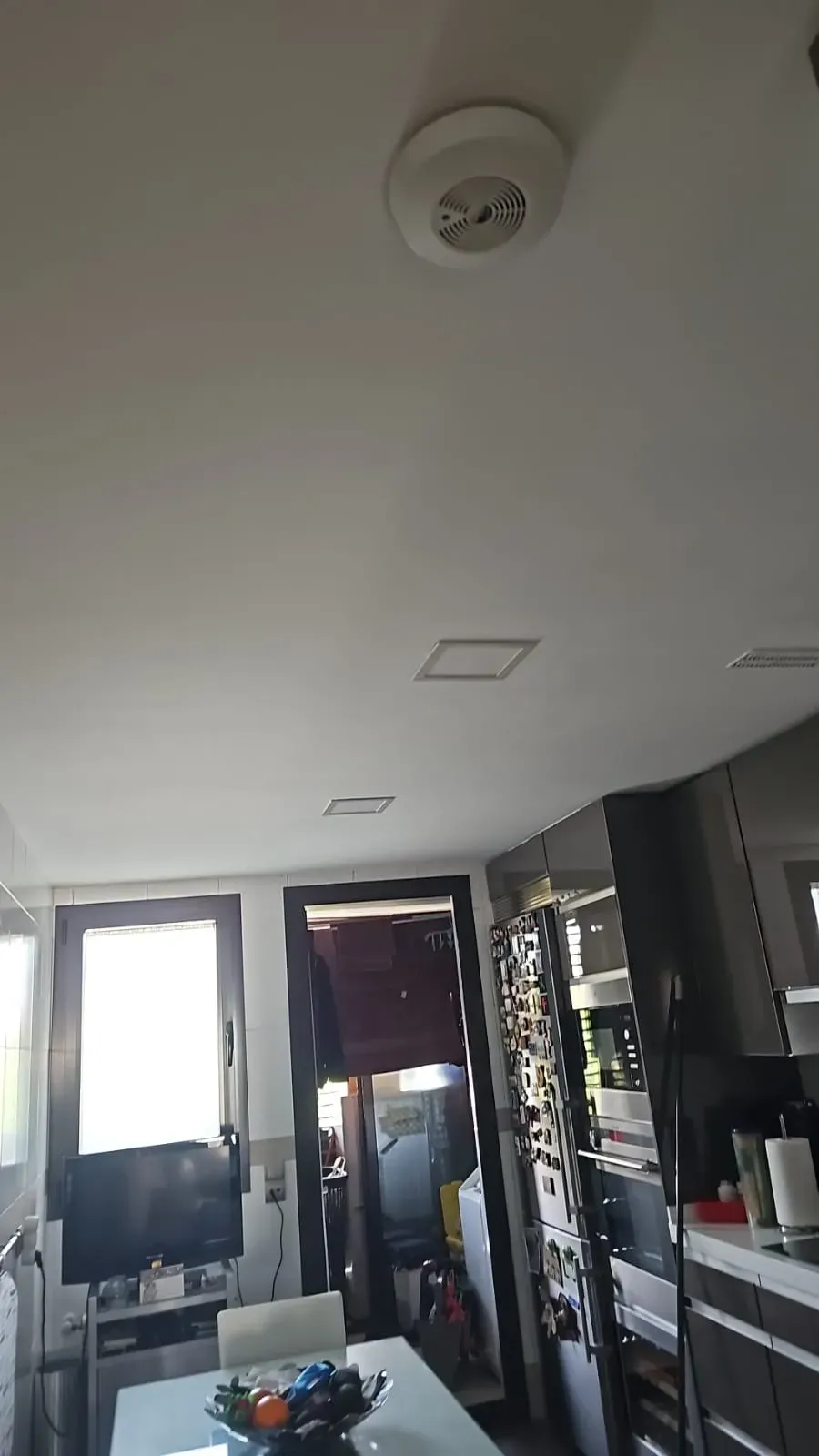 Interior de cocina moderno con luces blancas en el techo, armarios oscuros y puertas de cristal en la parte trasera.
