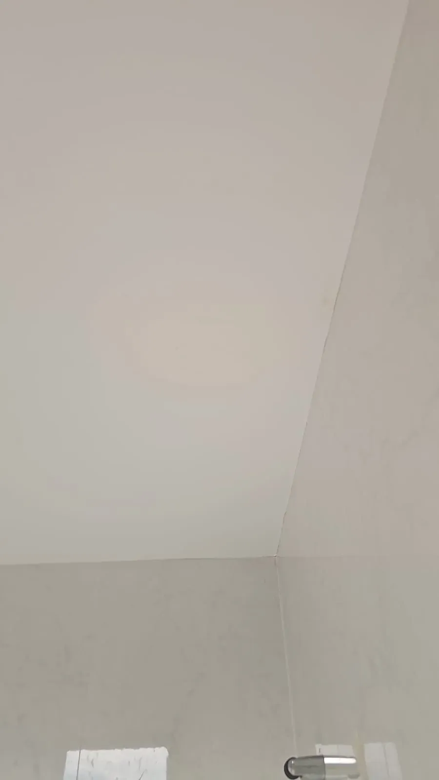 Rincón de habitación vacío con techo blanco, paredes gris claro y una pequeña lámpara de pared cerca de la parte inferior.