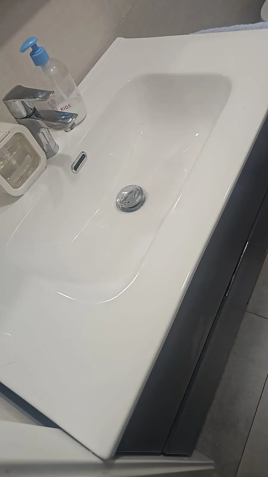 Lavabo blanco con grifo, dispensador de jabón y tapón de desagüe sobre una encimera oscura.