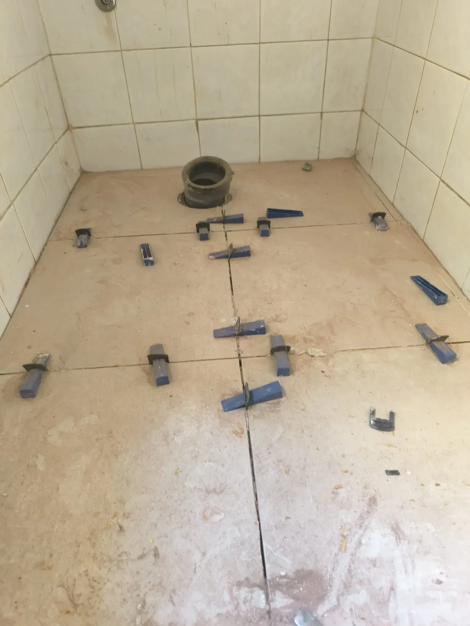 Suelo de ducha alicatado con separadores azules dispersos y una abertura de desagüe, a mitad de la instalación.