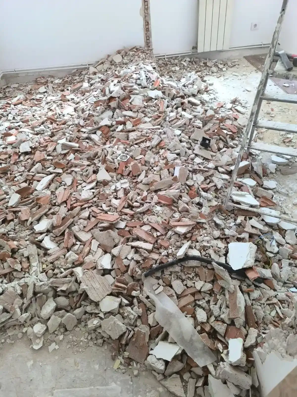 Montón de escombros y ladrillos rotos dentro de una habitación, con una escalera a la derecha.