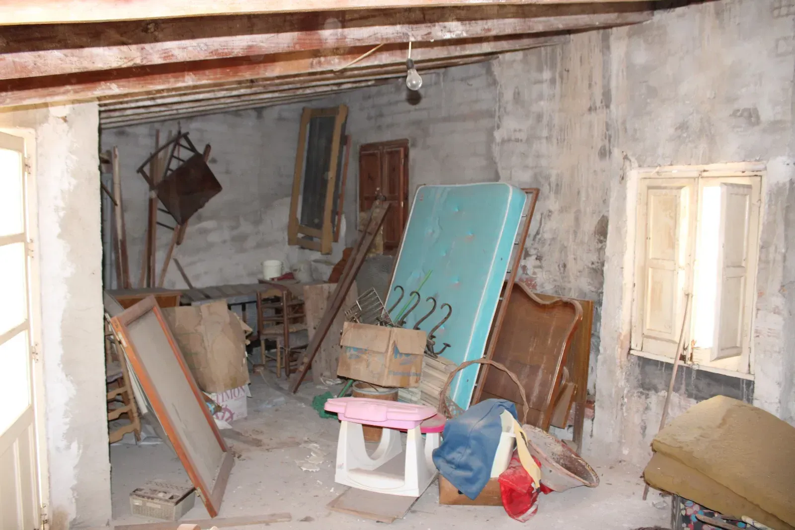 Habitación desordenada y polvorienta, con muebles rotos, una tabla turquesa y escombros de construcción esparcidos.