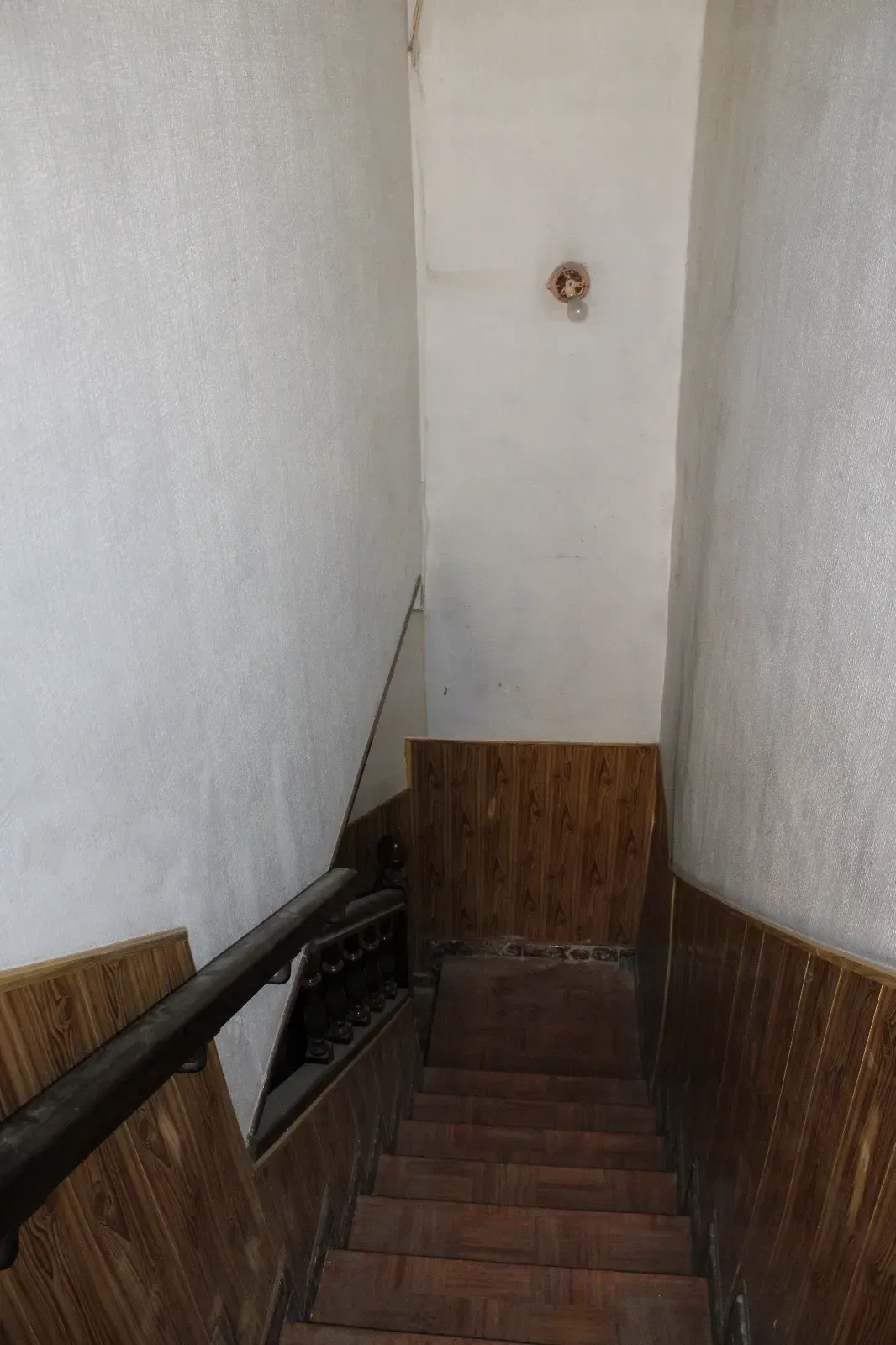 Estrecha escalera interior que desciende a una planta inferior, con paredes blancas y revestimiento de madera oscura.