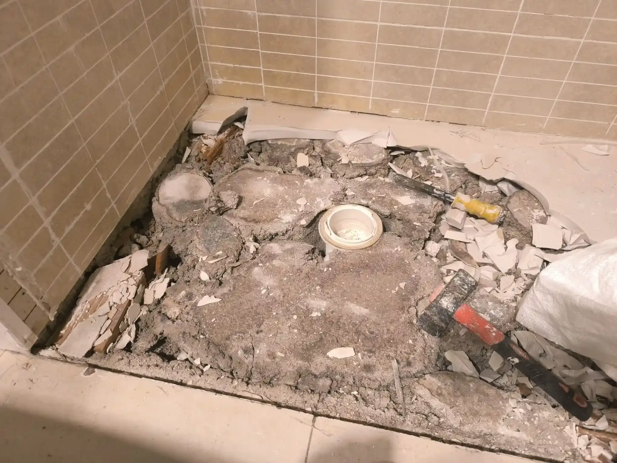 Área del lavabo del baño dañada, con azulejos rotos, escombros y tuberías expuestas.