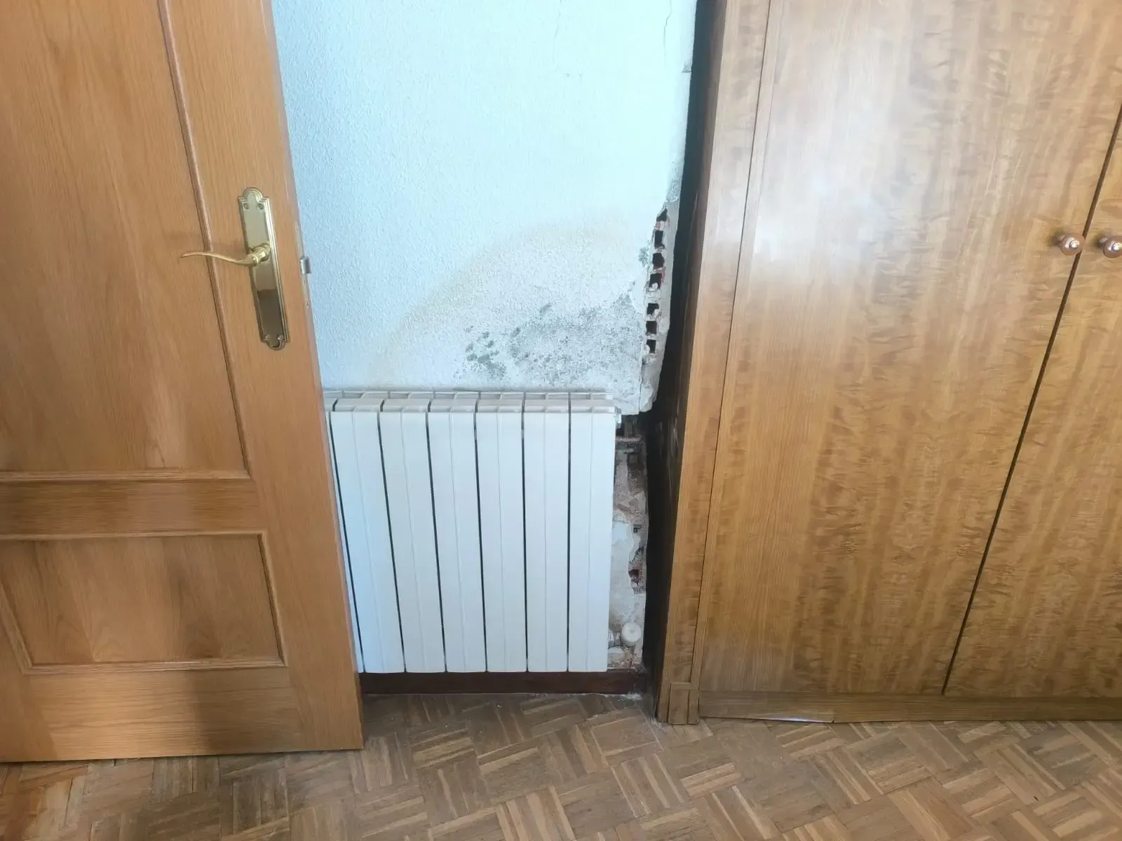 Entrada abierta con un radiador blanco y moho negro visible en la pared encima.