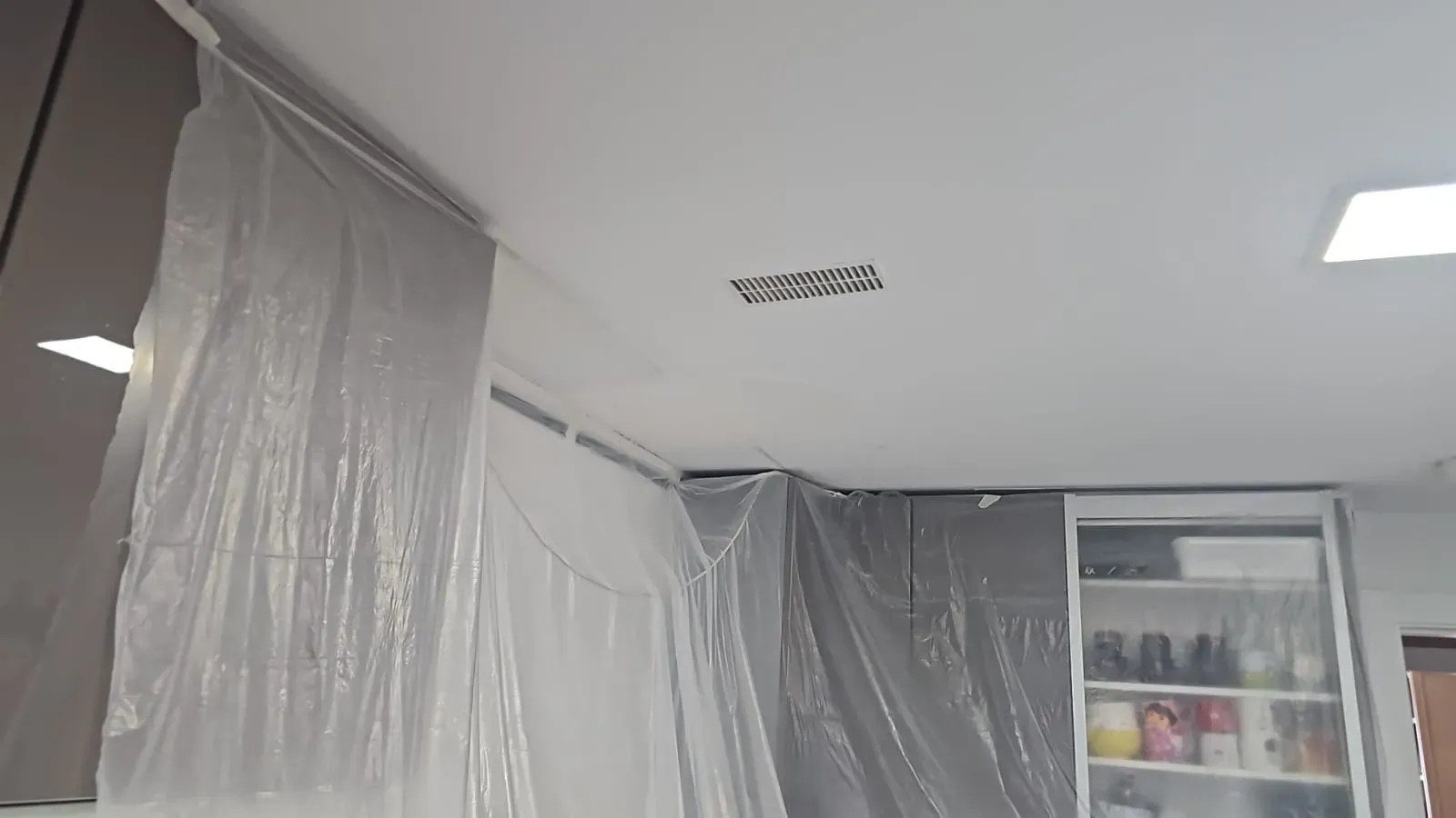 En una habitación, cerca de un armario con suministros, hay una zona del techo cubierta con una lámina de plástico colgante.