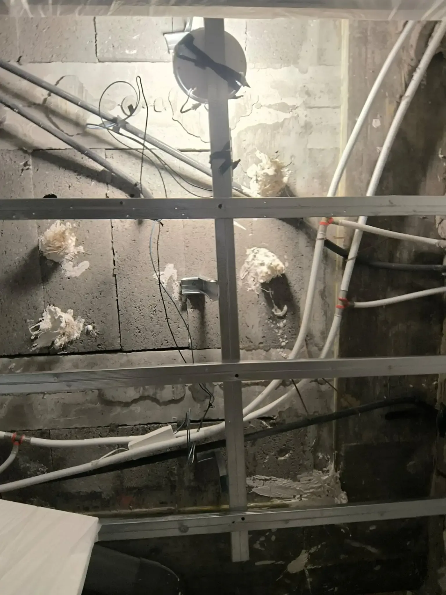 Techo industrial con tuberías y vigas a la vista, y una luz cenital brillante sobre una pared de hormigón.