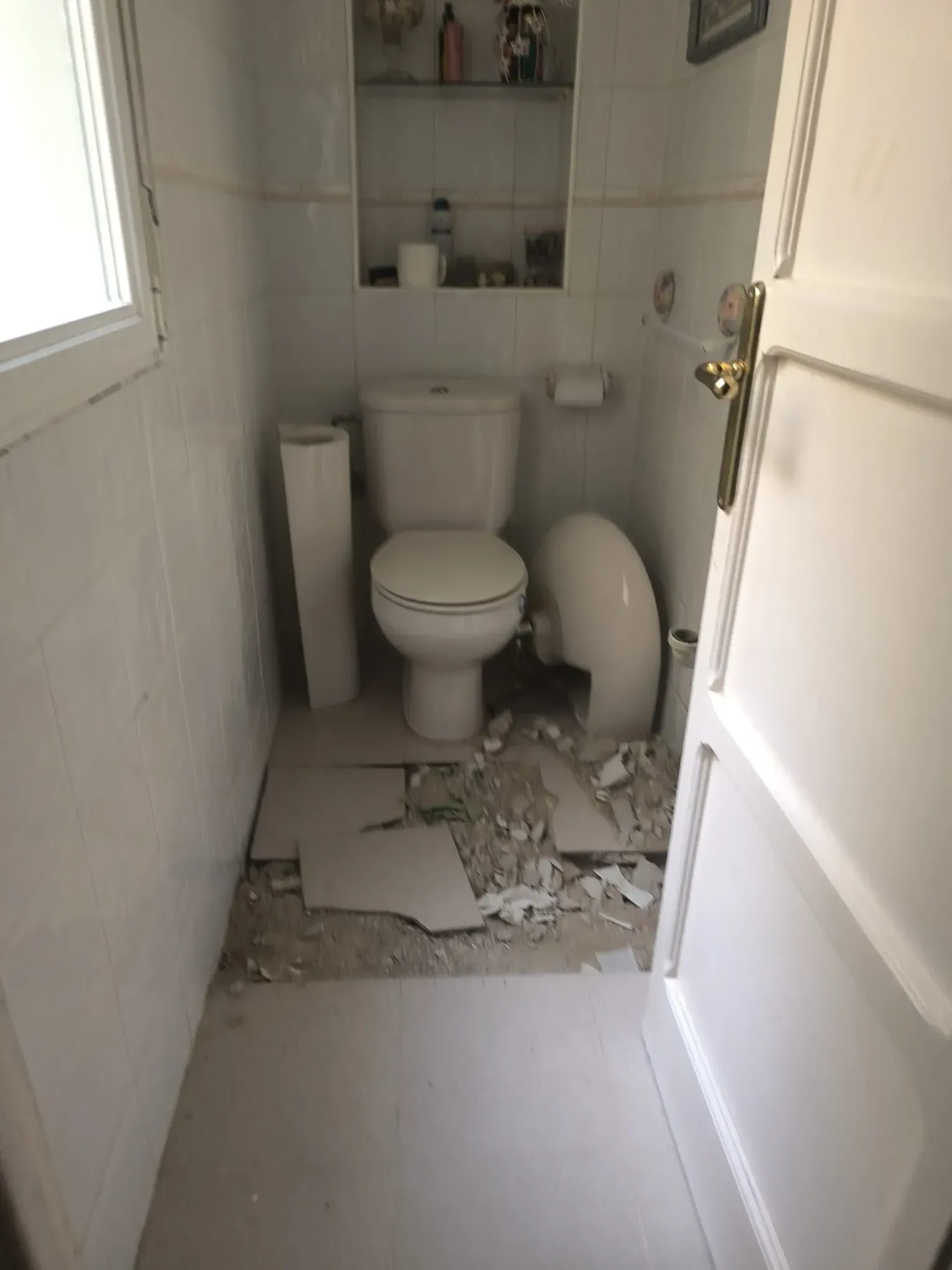 Baño dañado con baldosas rotas y escombros alrededor del inodoro y el lavabo.