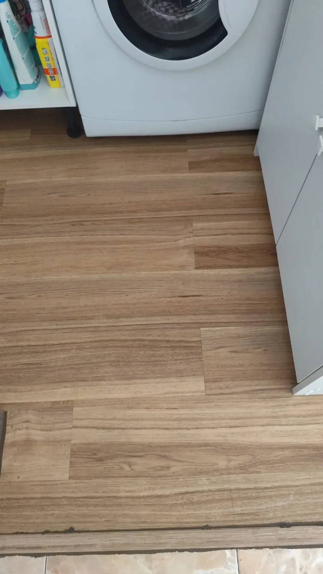 Suelo de madera en un cuarto de lavado junto a una lavadora y un armario blanco.