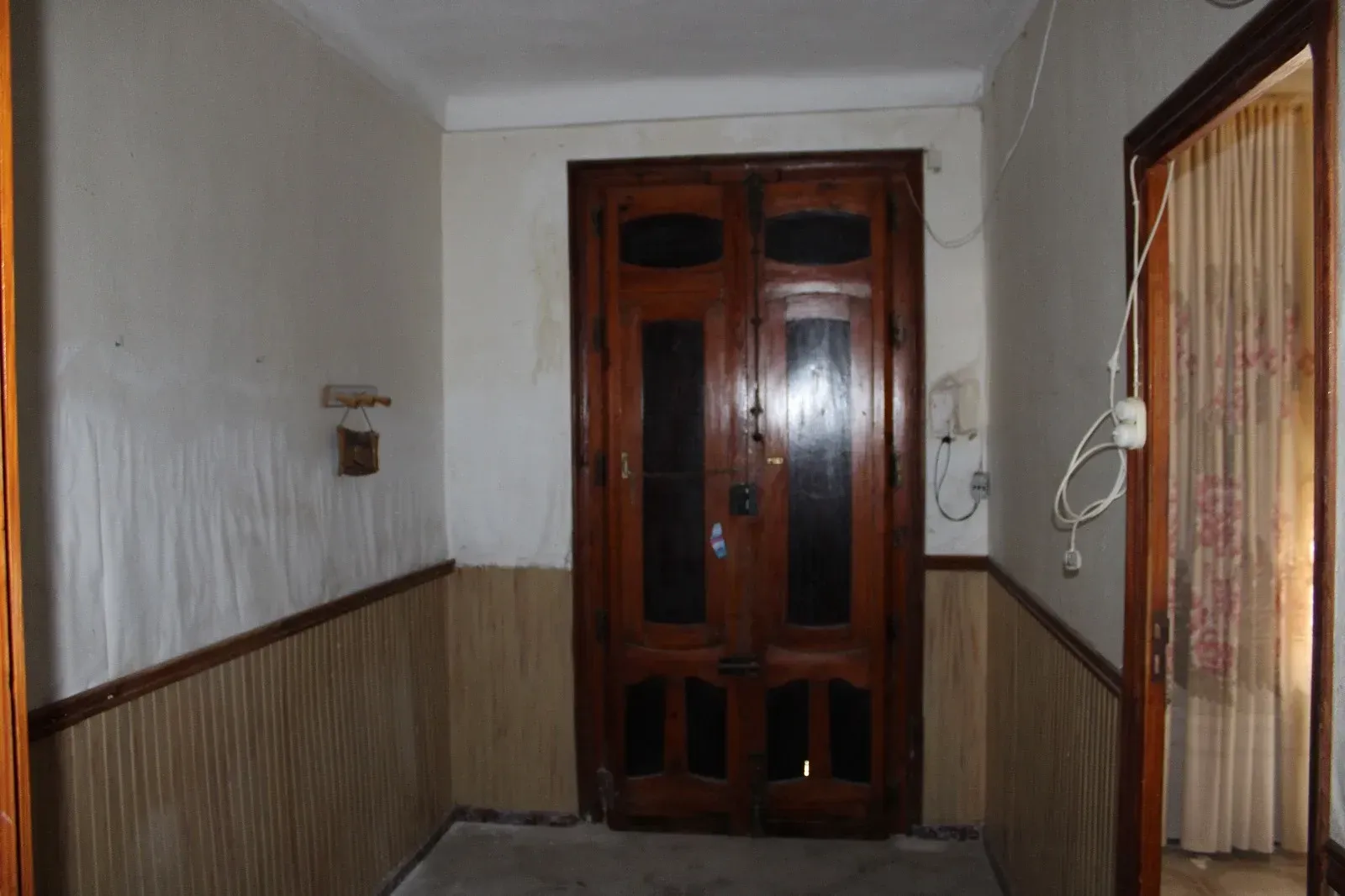 Pasillo estrecho con revestimiento de madera y una puerta principal de madera brillante al final.
