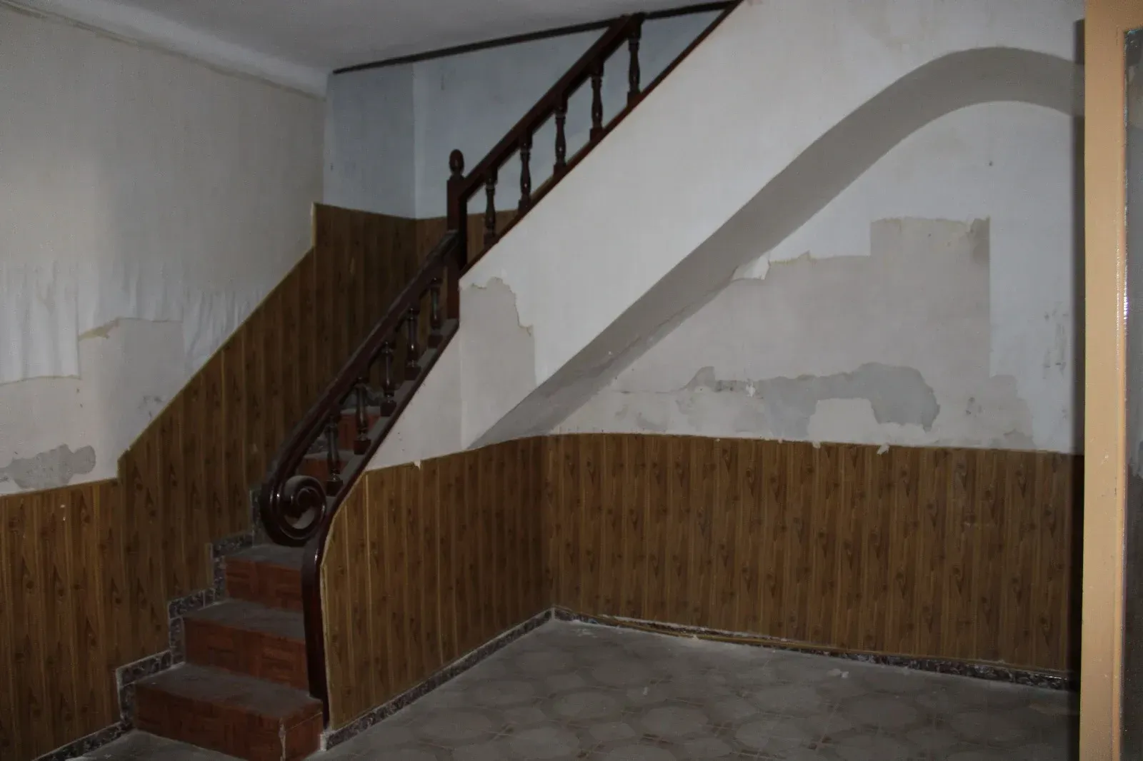 Escalera interior vacía con paredes revestidas de madera y yeso blanco desgastado.