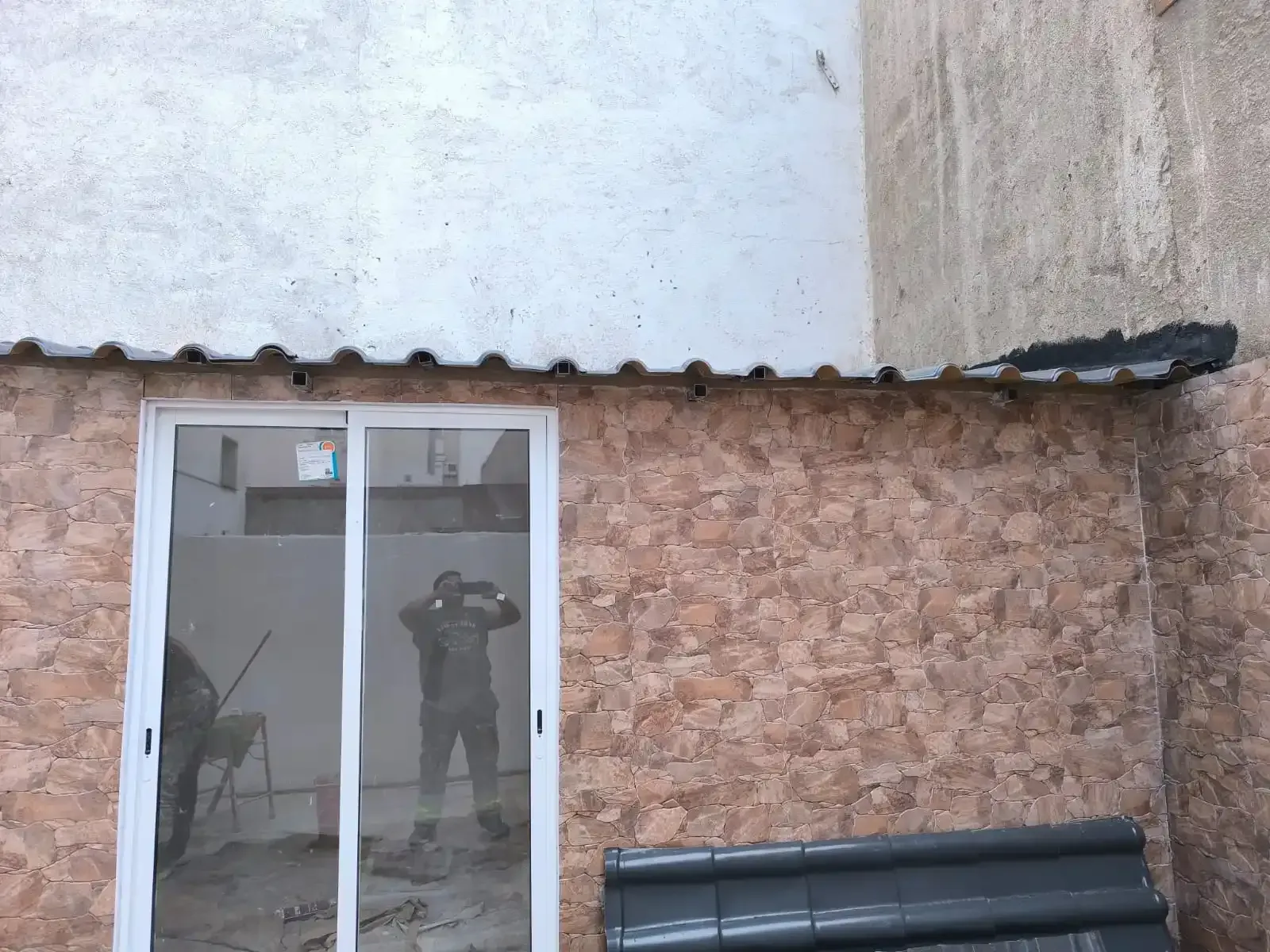 Puerta corrediza de cristal en un edificio de piedra con una persona reflejada en el cristal y neumáticos apilados cerca.