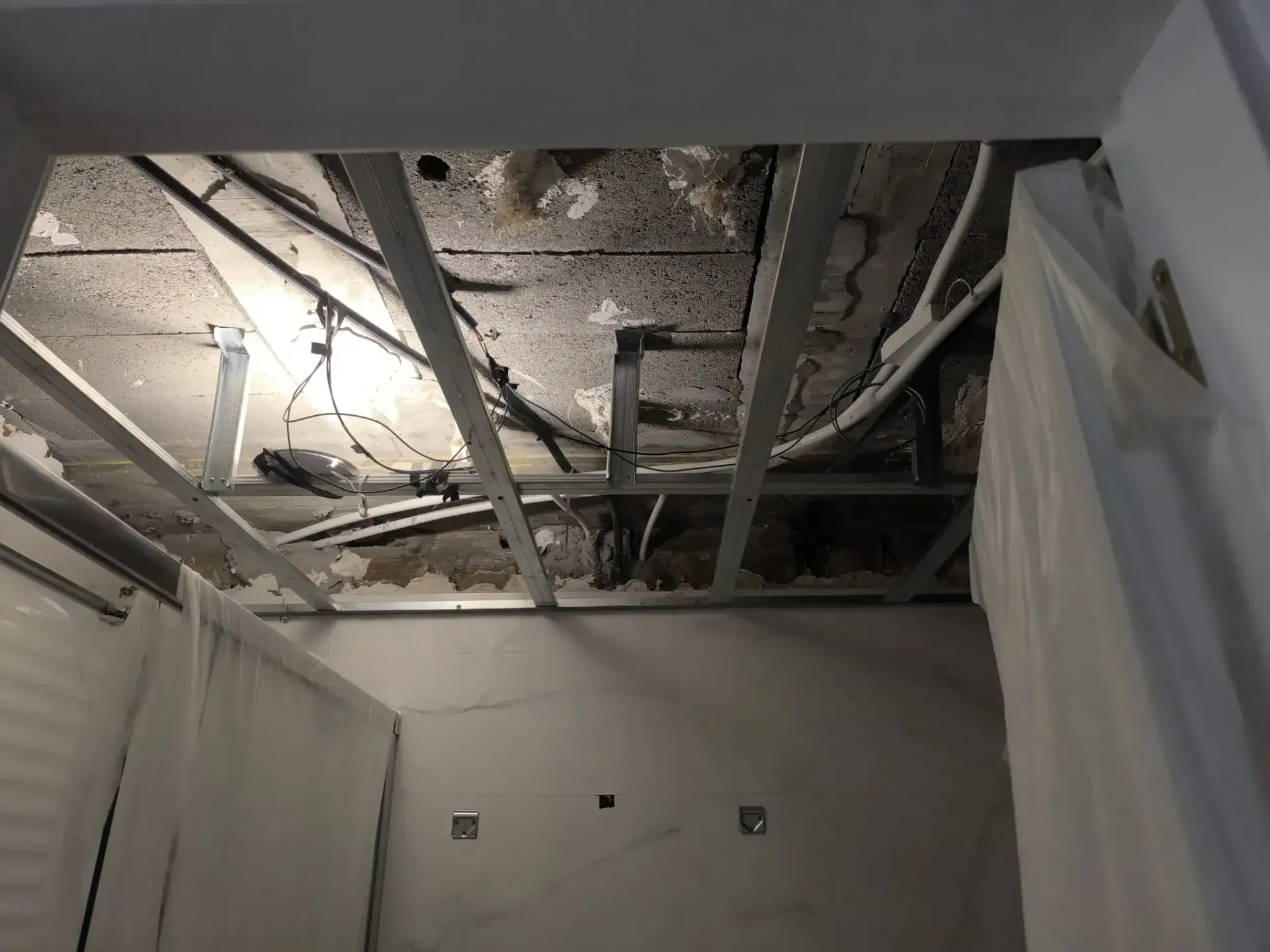 Techo dañado con vigas expuestas, aislamiento y escombros en una habitación en reparación.