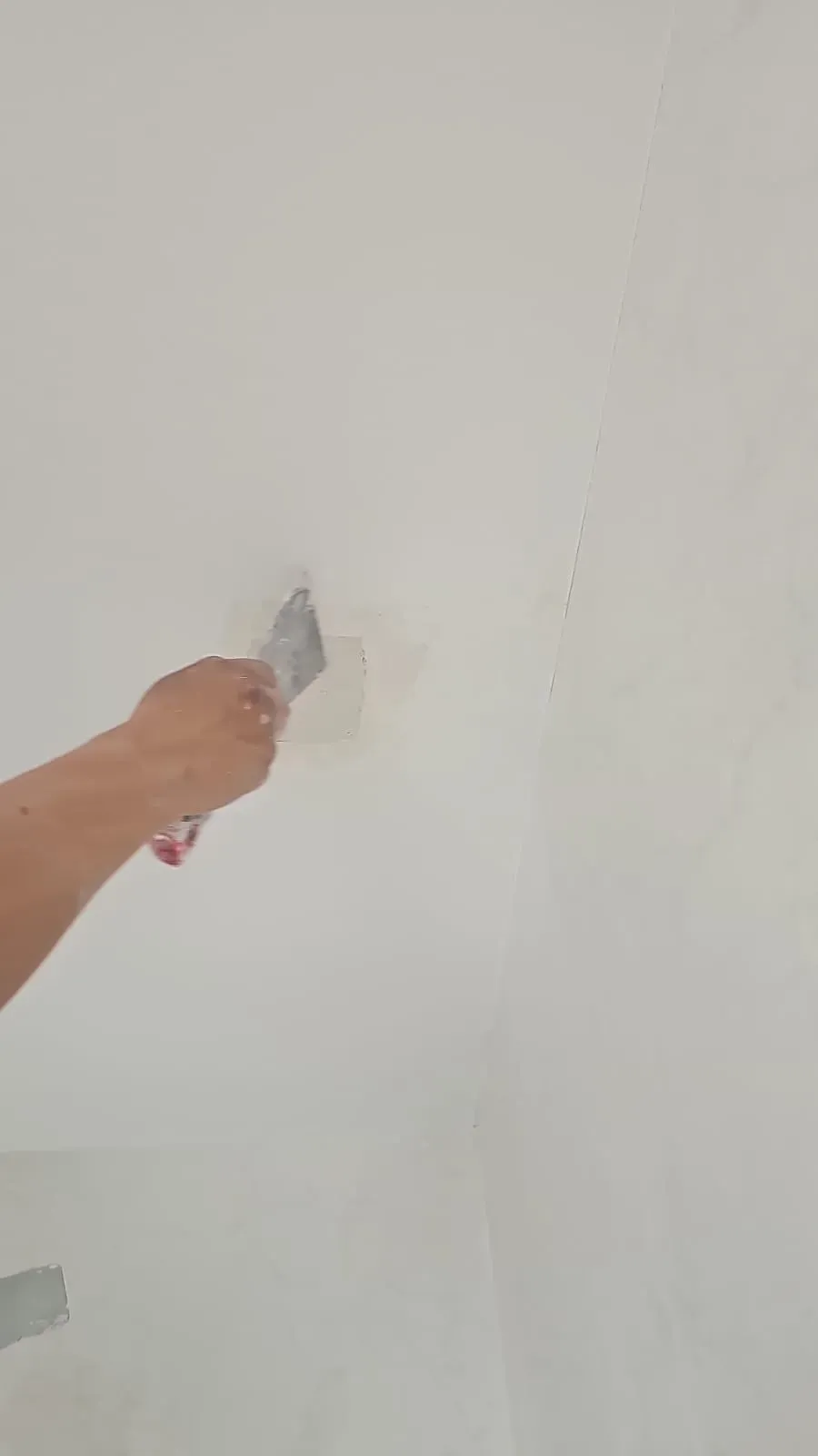 Una mano utiliza una espátula para tapar un pequeño agujero en una pared blanca.