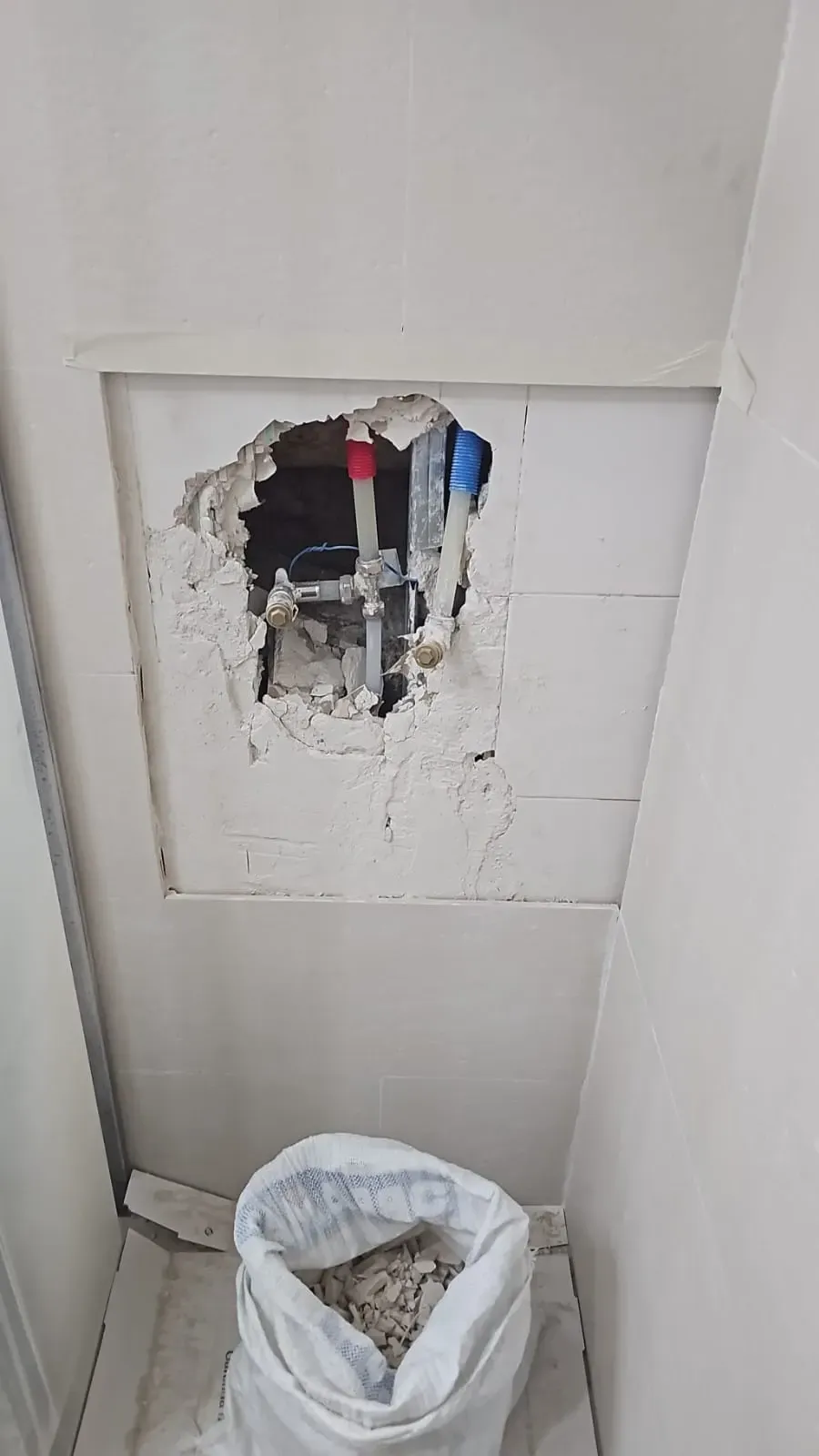 Panel de pared blanco dañado con un gran agujero que deja al descubierto cables rojos y azules