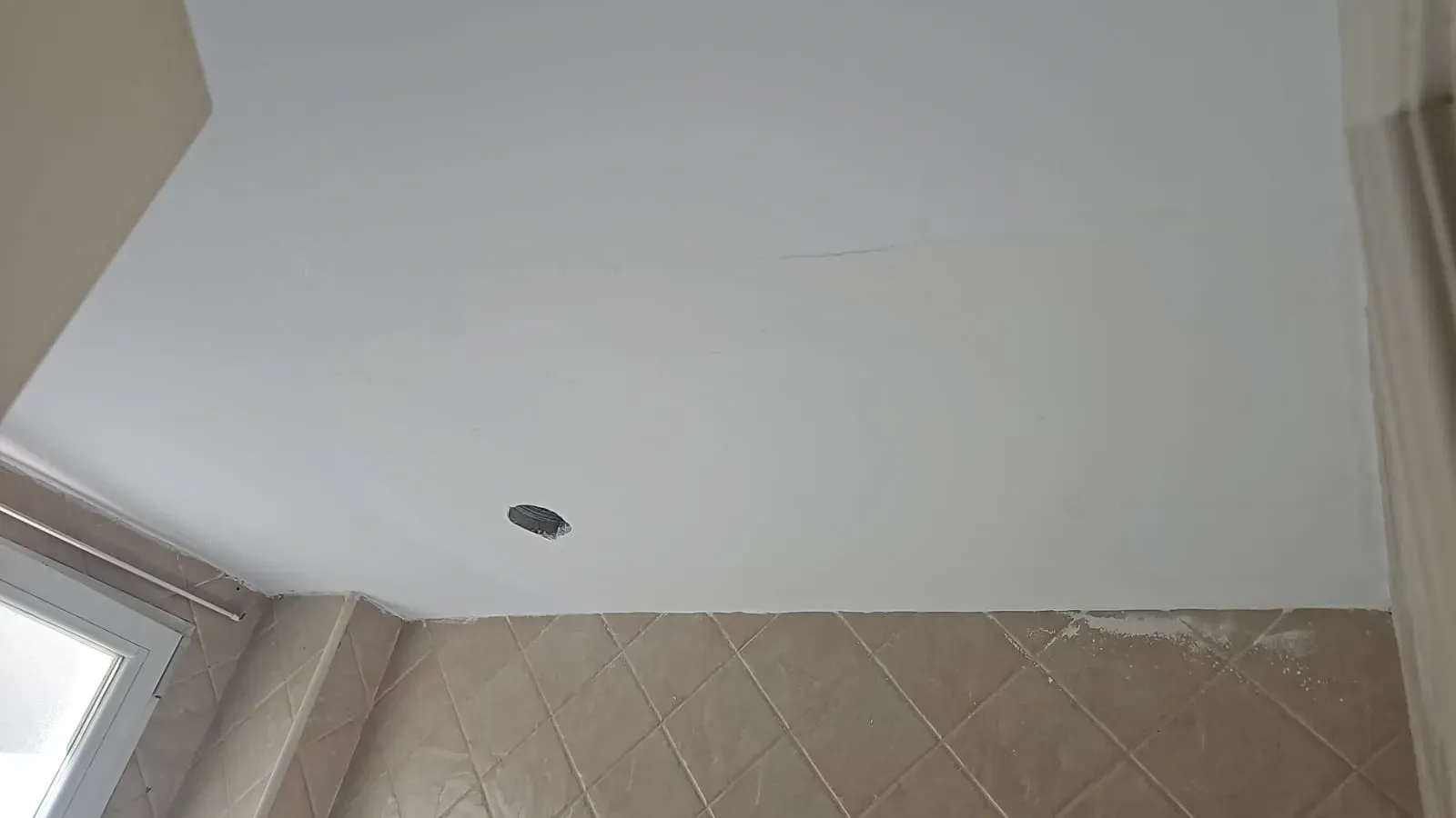 Techo blanco y esquina de pared alicatada con una pequeña abertura para luz empotrada.