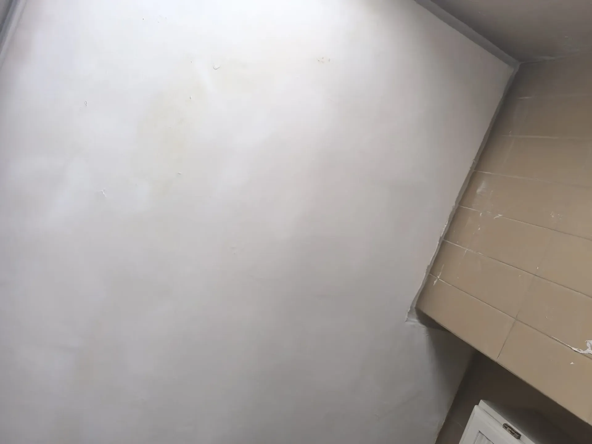 Primer plano de una pared gris claro y un techo de esquina con azulejos beige.