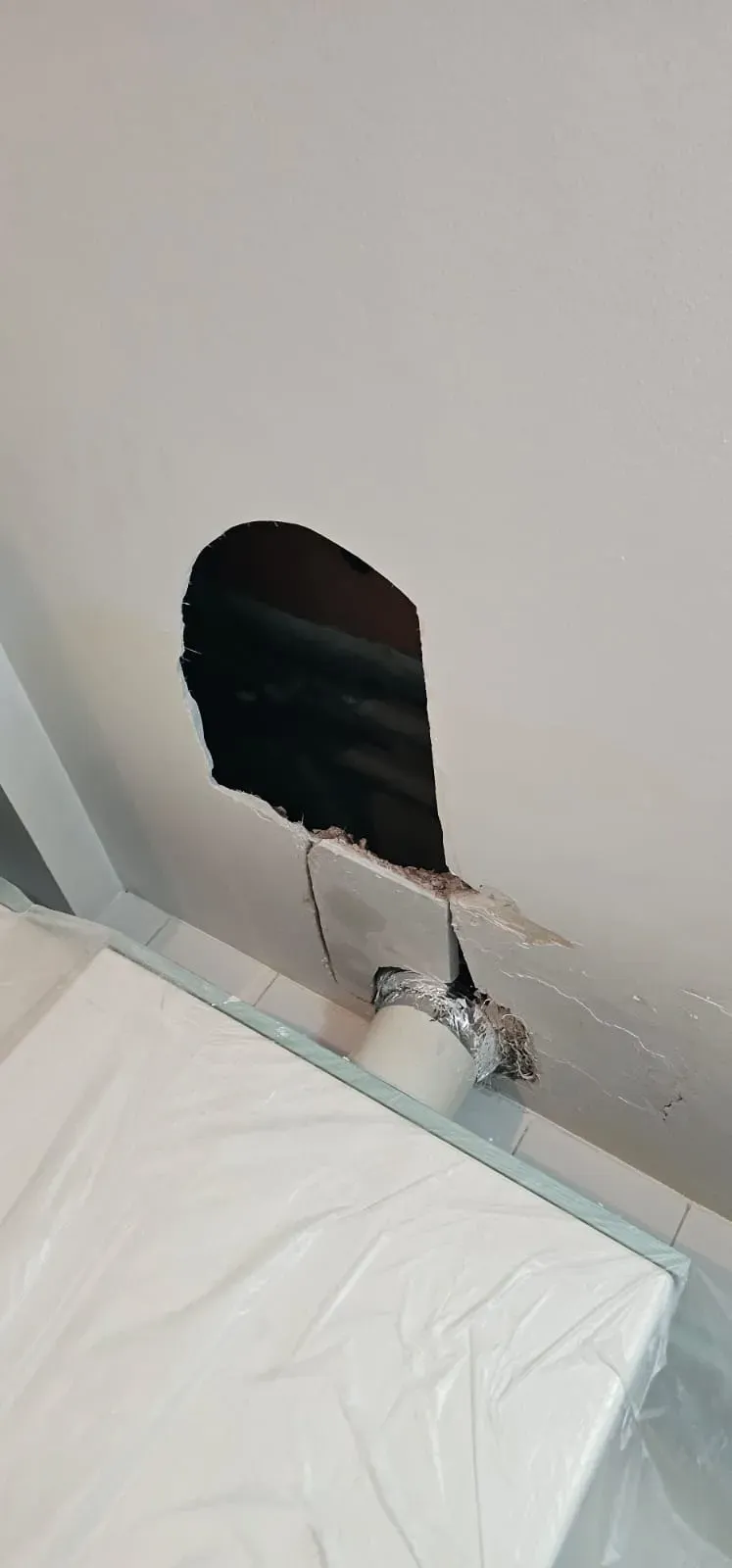 Daños en la pared con un gran agujero encima de una cama blanca, que deja al descubierto el interior y los escombros.