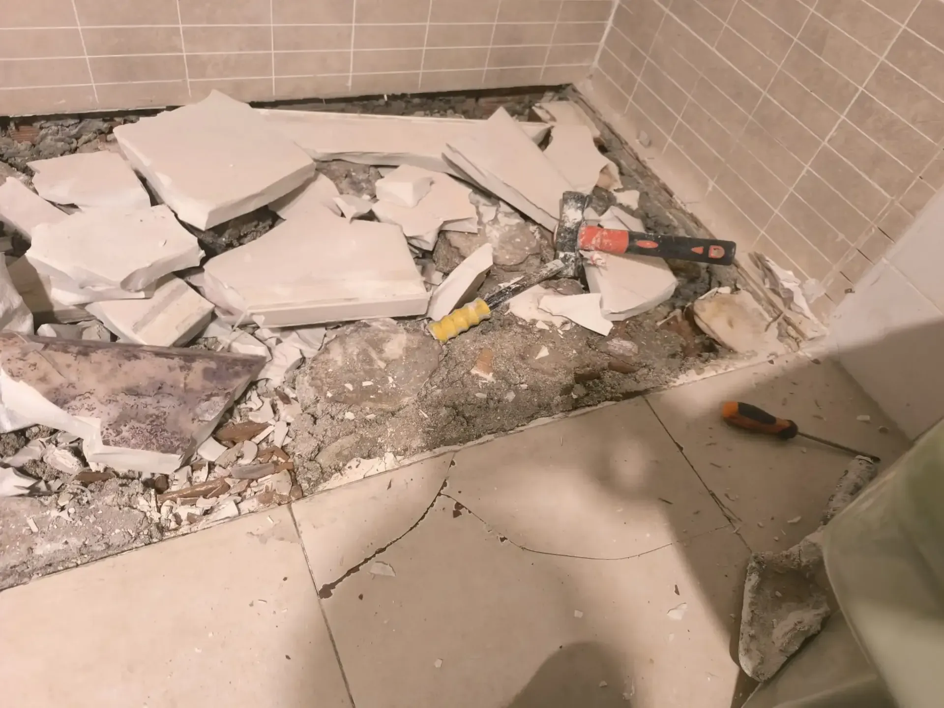 Trozos de baldosas blancas rotas y escombros esparcidos por el suelo de un baño, cerca de la ducha.