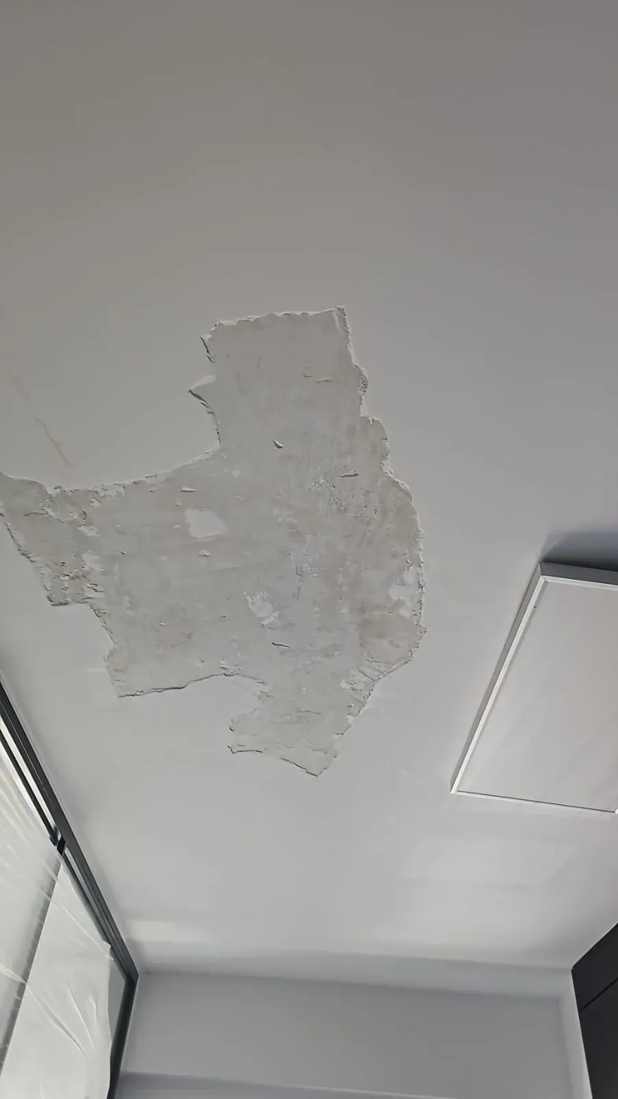Parche de pintura descascarada en un techo blanco cerca de una lámpara.