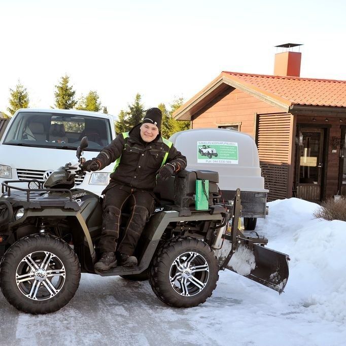 Henkilö istuu mönkijällä lumessa hytin ja pysäköidyn auton vieressä, hymyilee ja vilkuttaa.