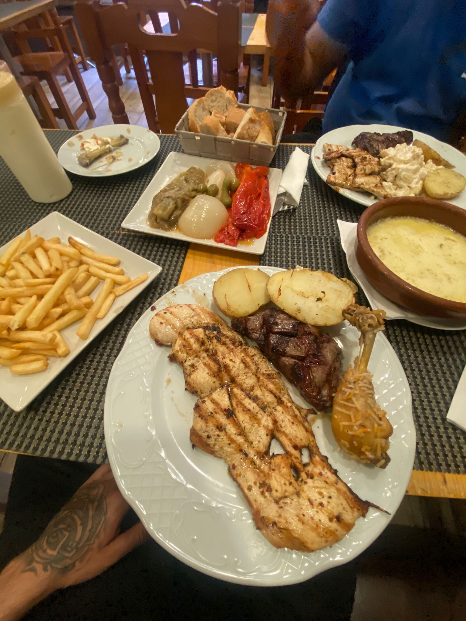 Plato principal con carne a la parrilla, patatas fritas, puré de patatas y sopa, servido en una mesa de comedor.