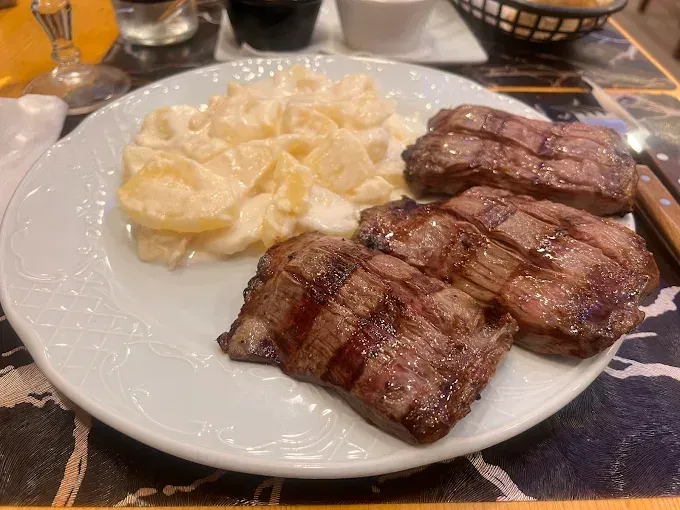 Filete a la parrilla con patatas cremosas en un plato blanco en la mesa de un restaurante.