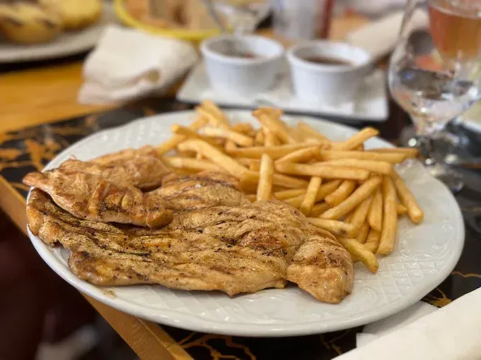 Pescado a la parrilla y patatas fritas en un plato blanco en la mesa de un restaurante.