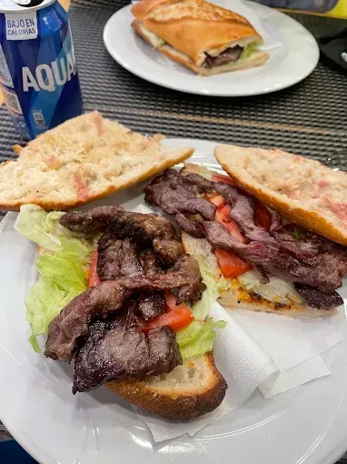 Sándwich abierto con carne a la parrilla y lechuga en un plato, con una botella azul de Aquafina cerca.