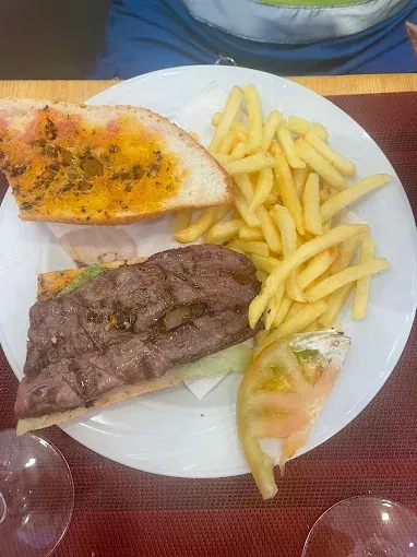 Plato de bistec, papas fritas y pan tostado con salsa de naranja sobre una mesa.