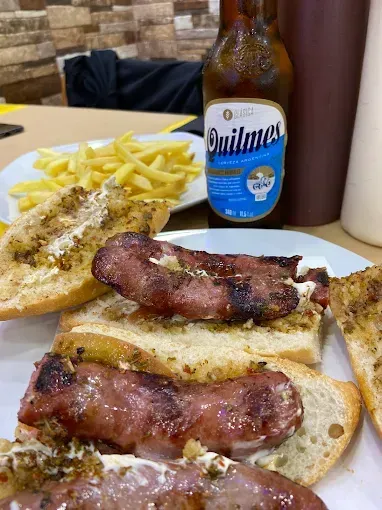 Plato de salchichas a la parrilla y pan con papas fritas, salsa para mojar y una botella de cerveza Quilmes