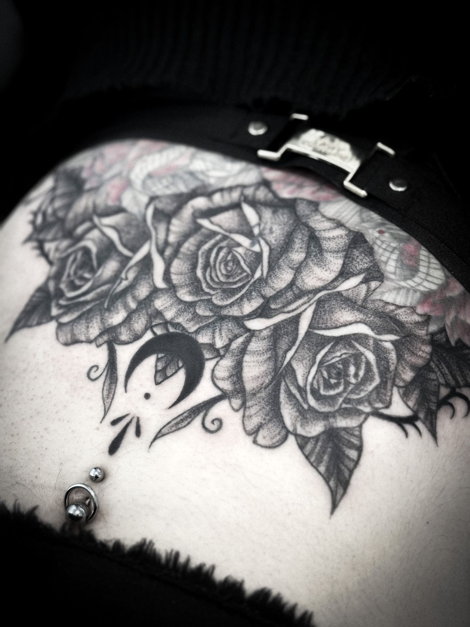 Tatuaje de tres rosas y una luna creciente con hojas; en la cadera cerca de un ombligo perforado.