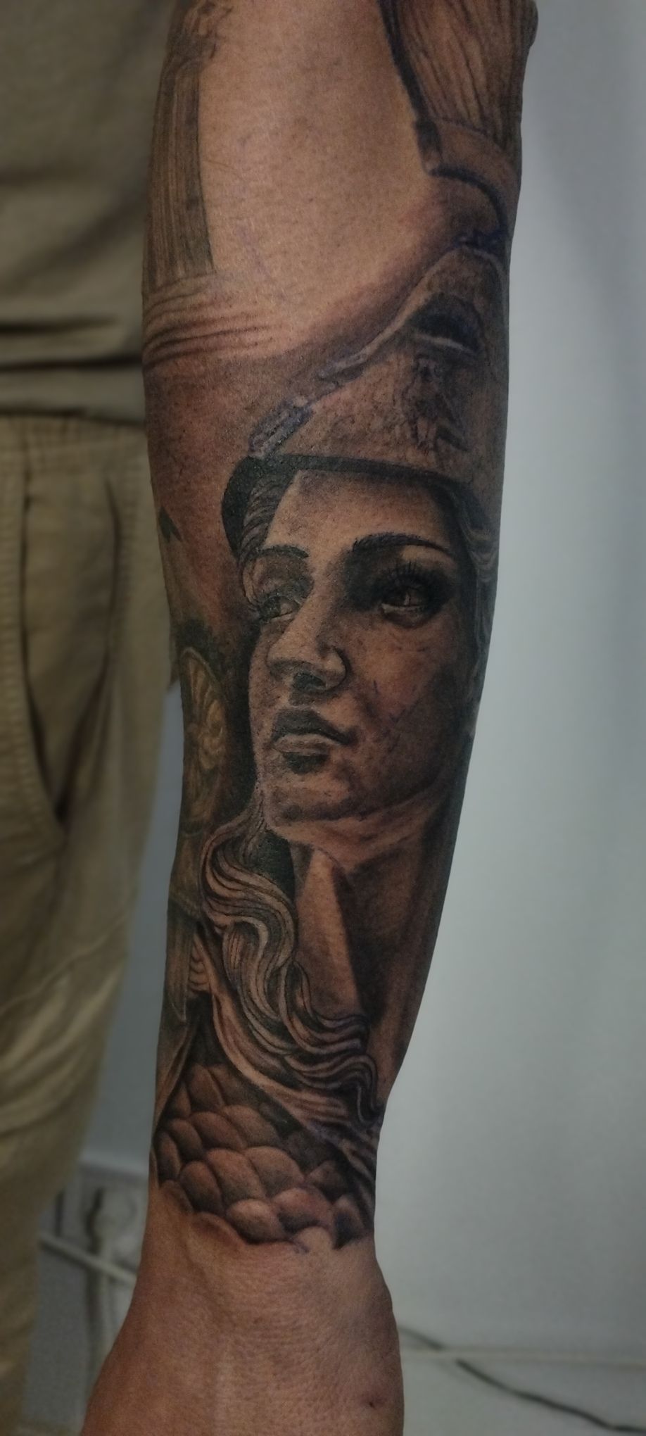 Tatuaje de una mujer con un tocado y escamas en el antebrazo. Tinta negra y gris.