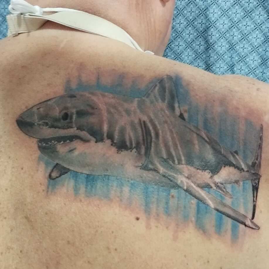 Tatuaje de tiburón en la espalda de una persona, con agua azul y detalles blancos.