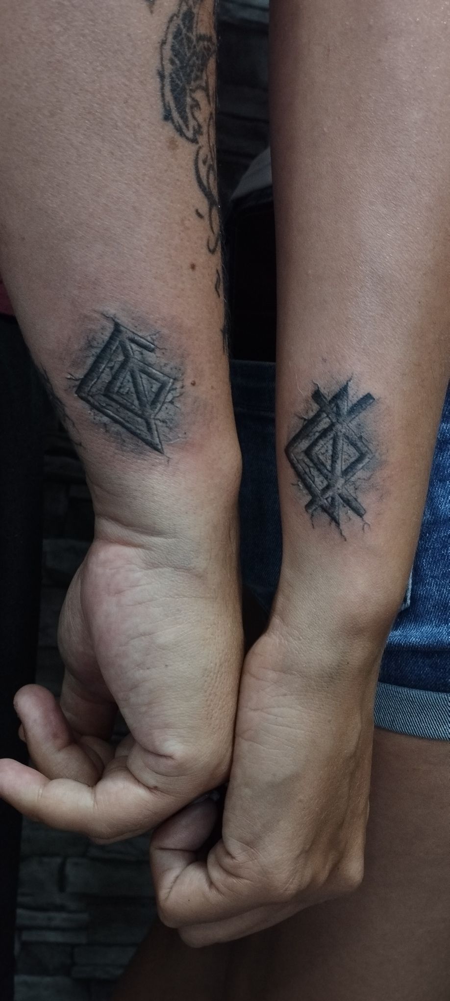 Dos muñecas con tatuajes geométricos a juego, una mano unida.