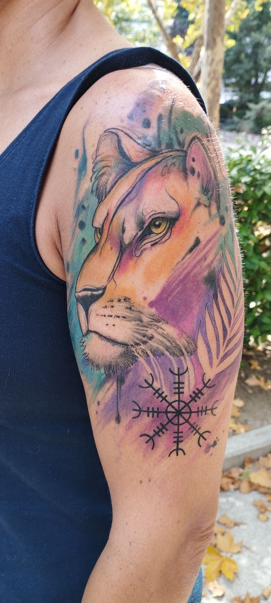 Tatuaje de leona en el brazo en estilo acuarela, con un símbolo islandés en la parte inferior.
