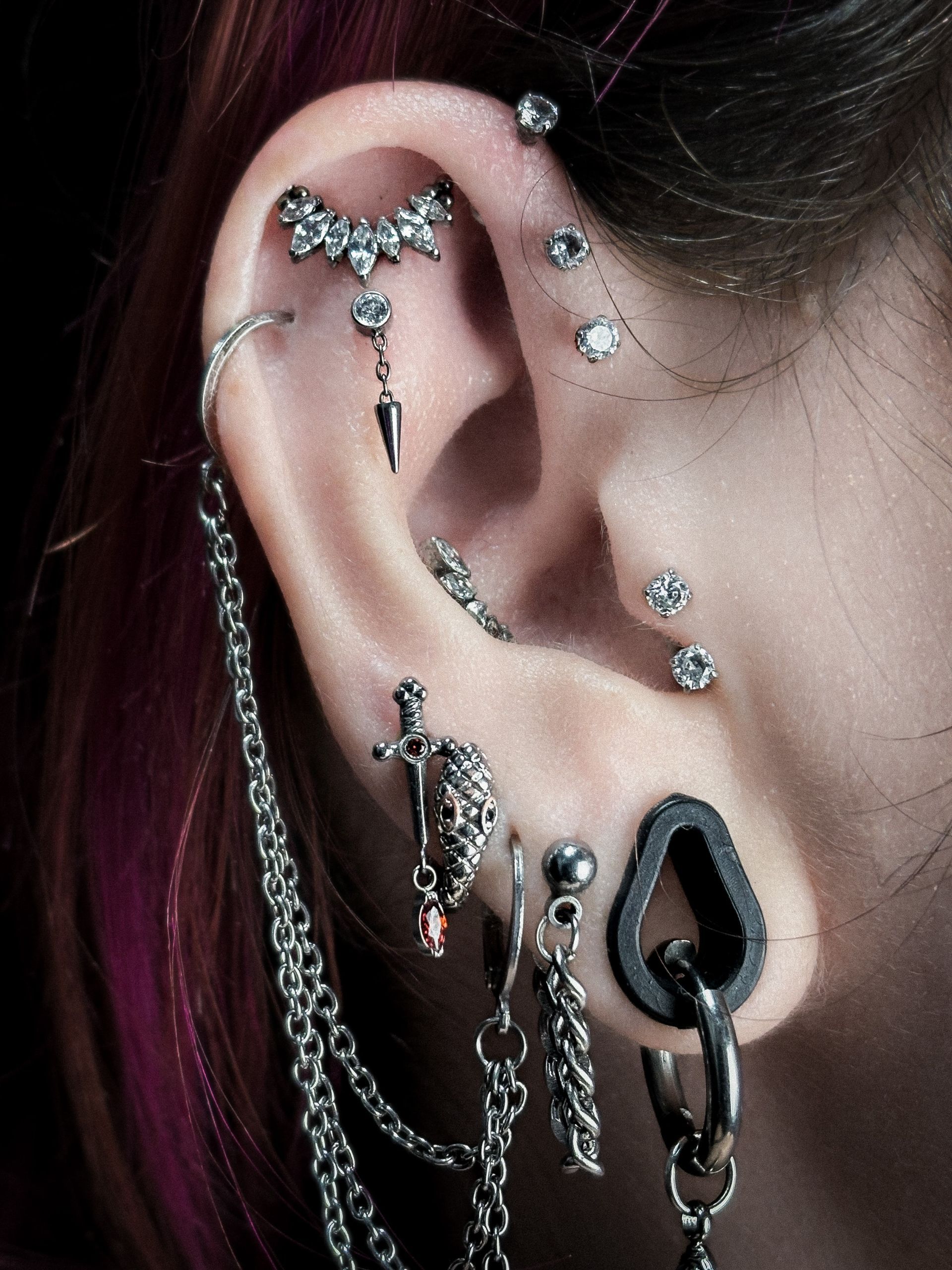 Primer plano de una oreja con múltiples perforaciones, incluidos tachuelas, una cadena y una lágrima colgante.