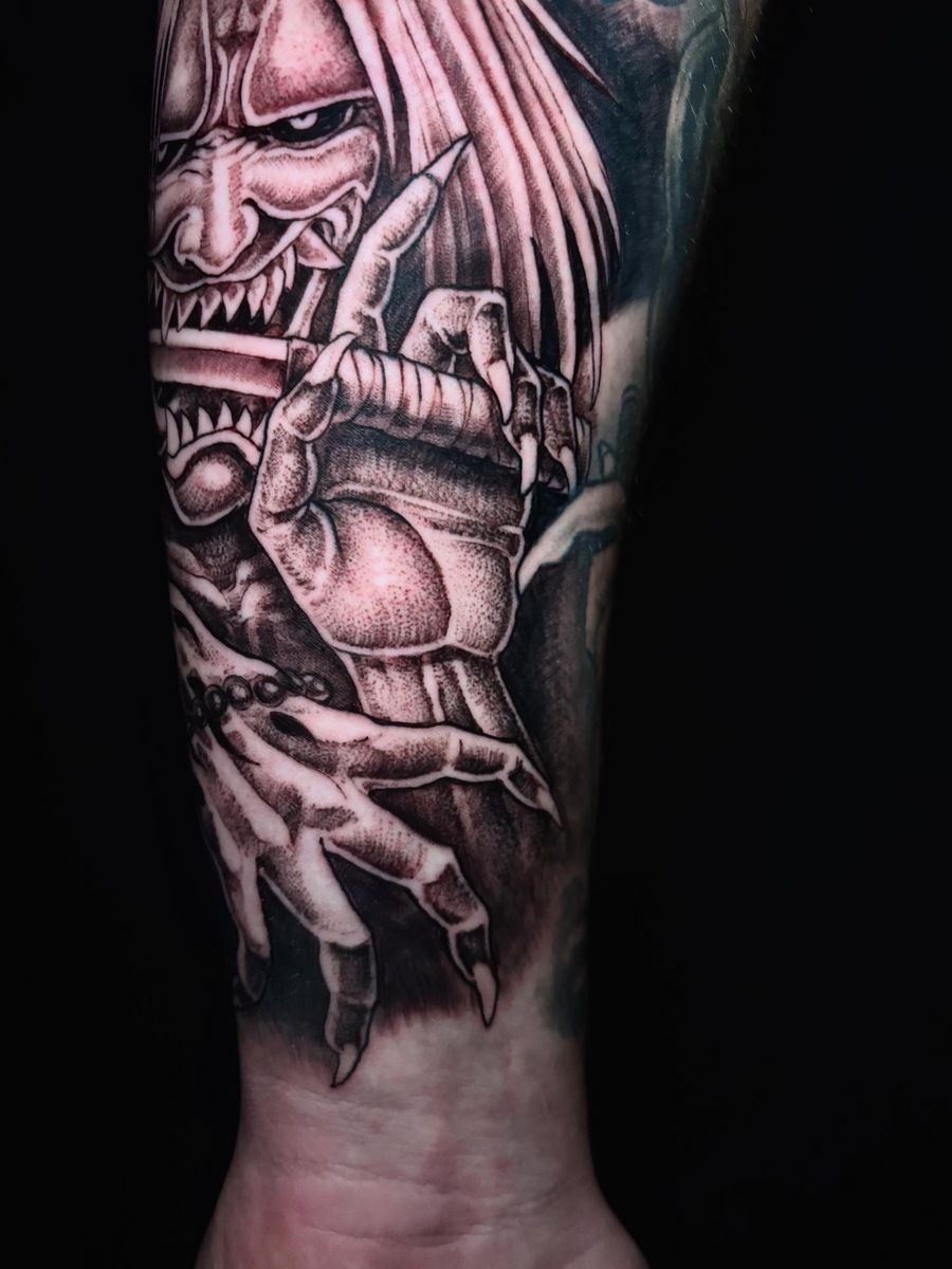 Tatuaje de una cara de demonio y una mano con garras extendiéndose, estilo blanco y negro en el brazo.