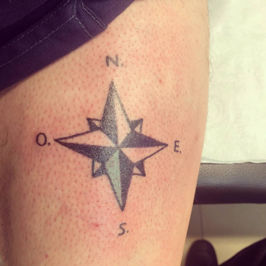 Tatuaje de rosa de los vientos en la piel, con N, O, E y S marcados. La zona central está sombreada.