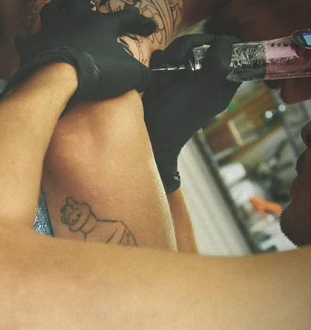 Persona haciéndose un tatuaje en el brazo, artista trabajando con una pistola de tatuaje.