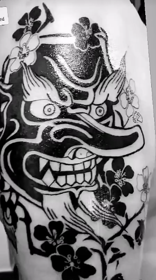 Tatuaje negro de una máscara japonesa Tengu con flores de cerezo en la piel.