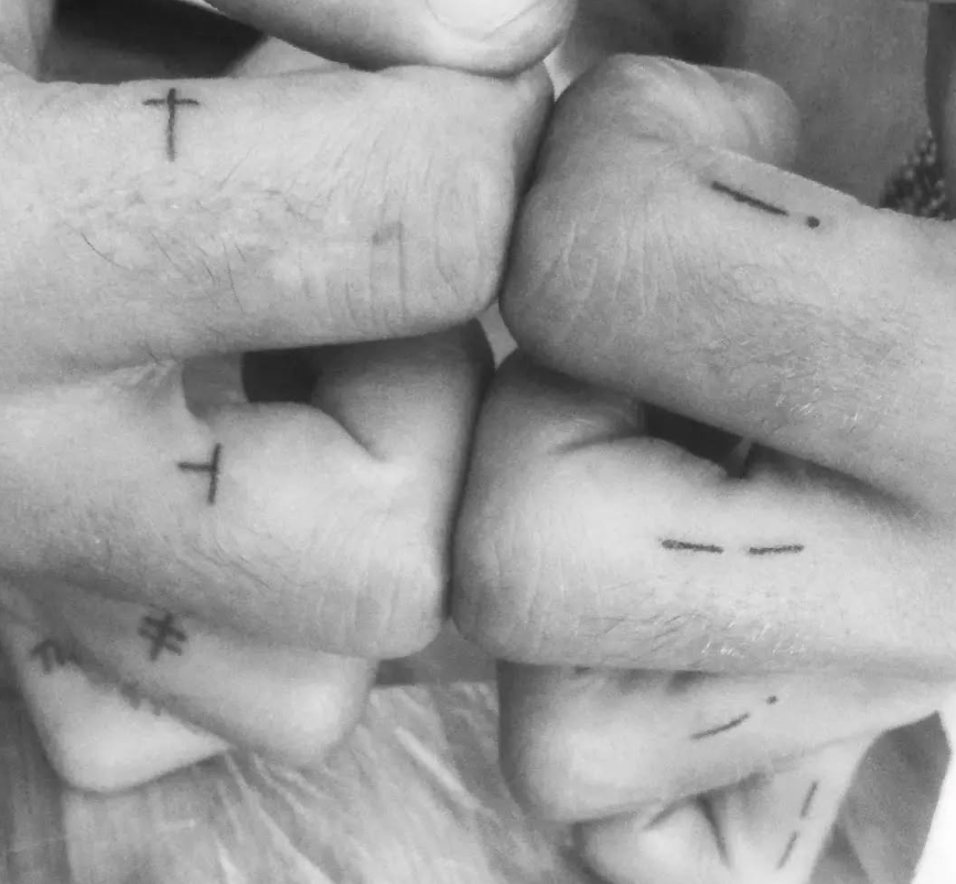 Cuatro manos tocándose, cada una con pequeños tatuajes: cruces y líneas.