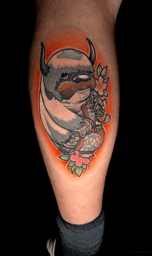 Tatuaje de Appa de Avatar: La Leyenda de Aang, con brillo naranja y flores.