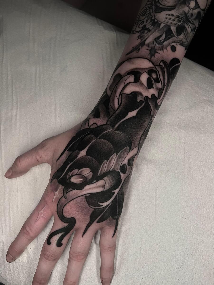 Tatuaje floral negro en una mano y muñeca, con sombreado detallado y líneas fluidas.