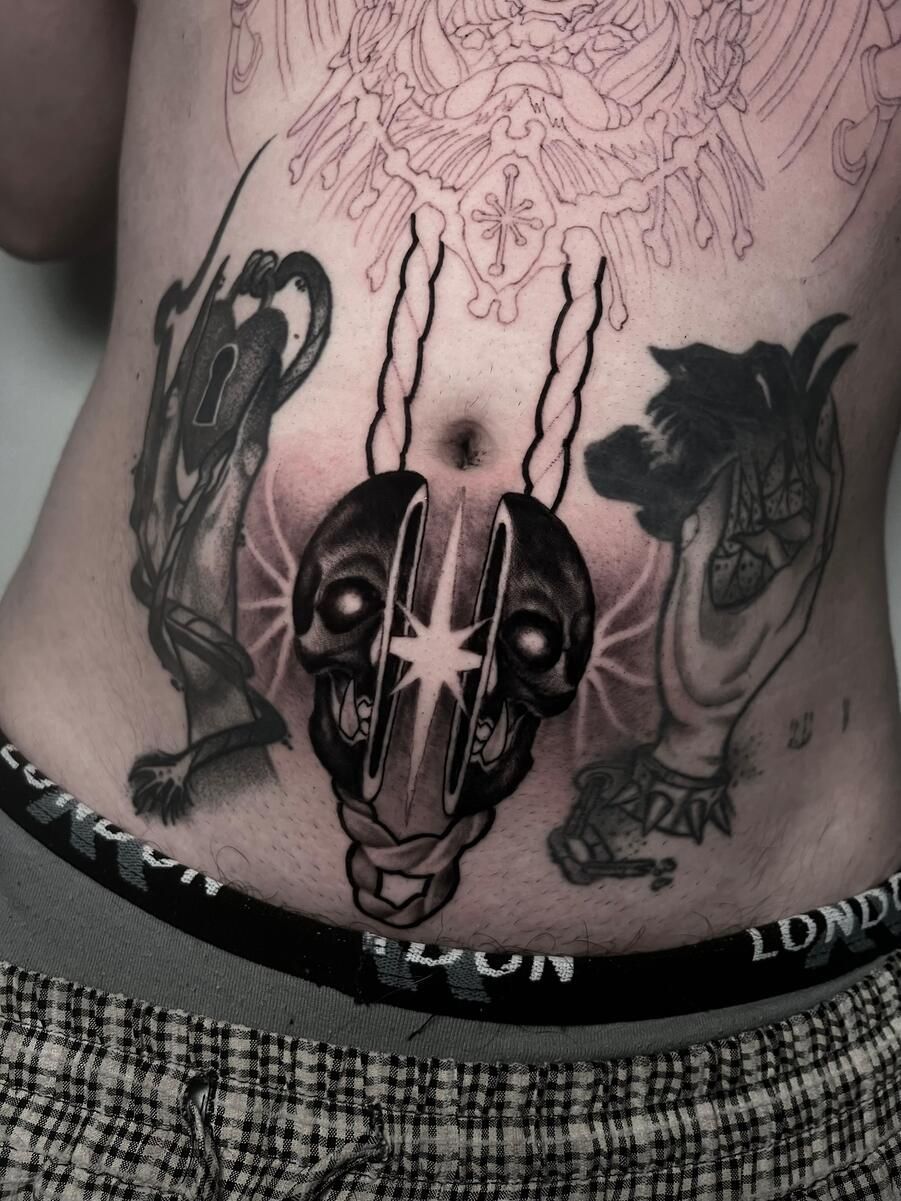 Tatuaje en el torso: calavera dividida con estrella, dos manos adornadas a cada lado y diseño esbozado arriba.