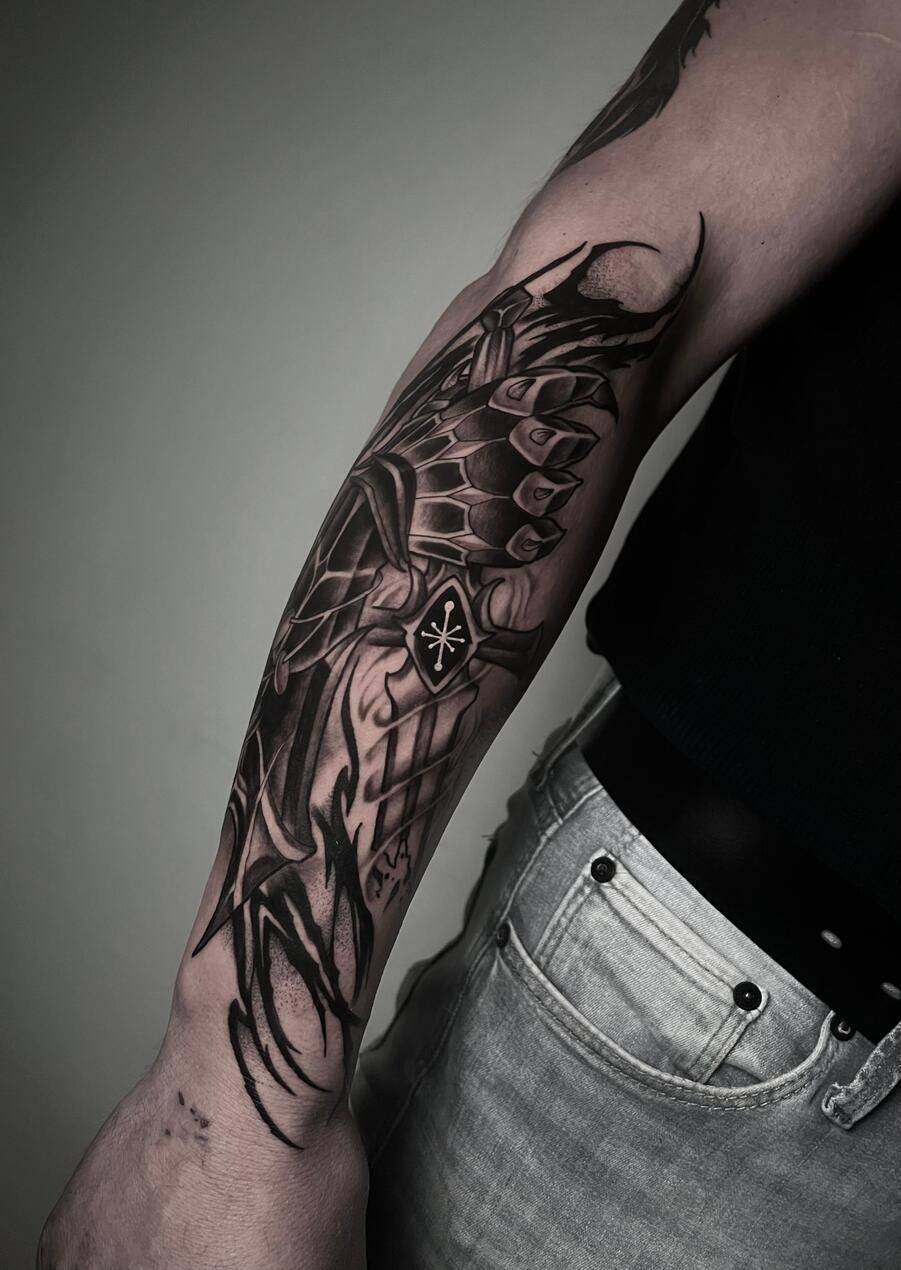 Brazo con manga de tatuaje detallada en negro y gris; diseño de caballero con una cruz.