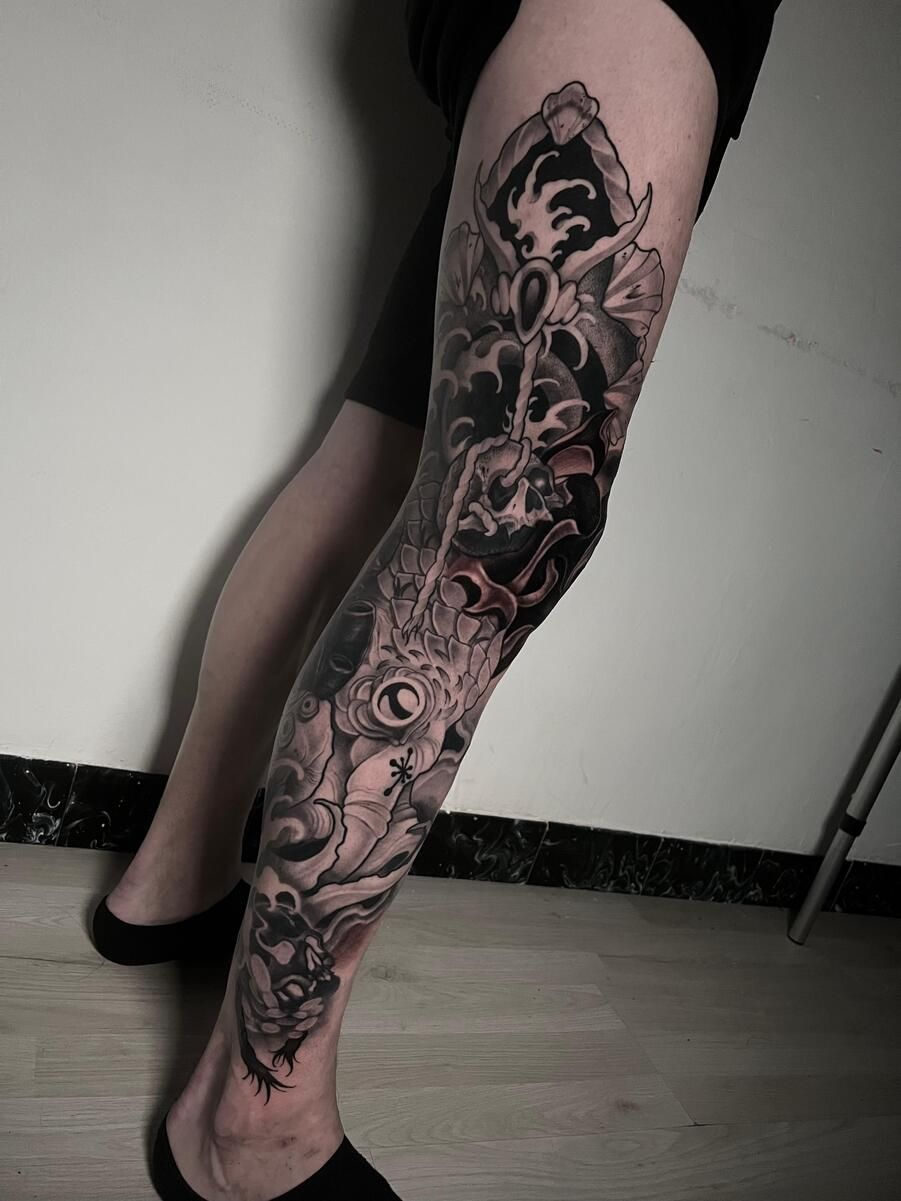 Pierna con una manga de tatuaje detallada en negro y gris; las imágenes complejas incluyen una calavera y formas orgánicas.