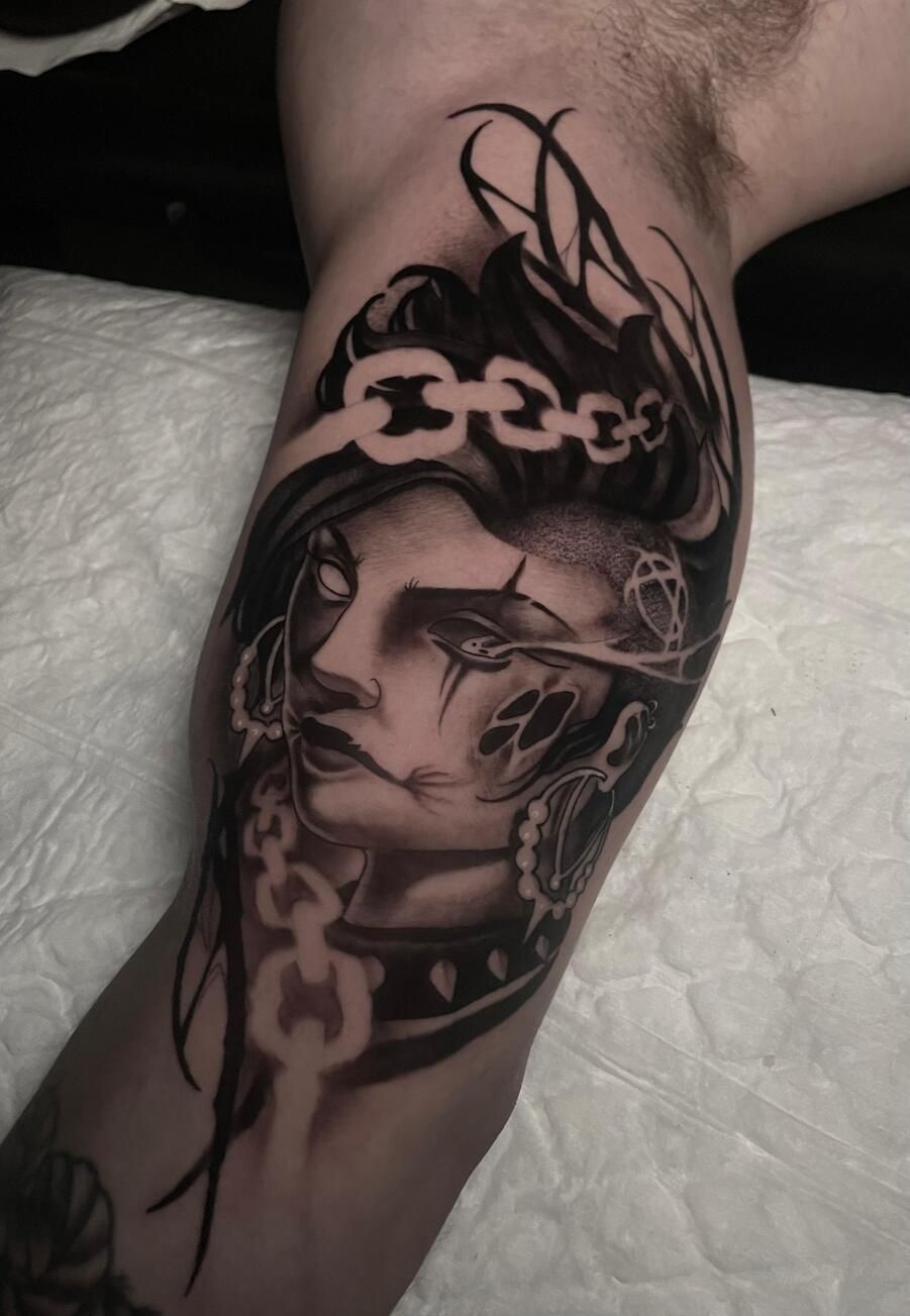 Tatuaje de un rostro de mujer con detalles de cadena en un brazo en tinta negra y gris.