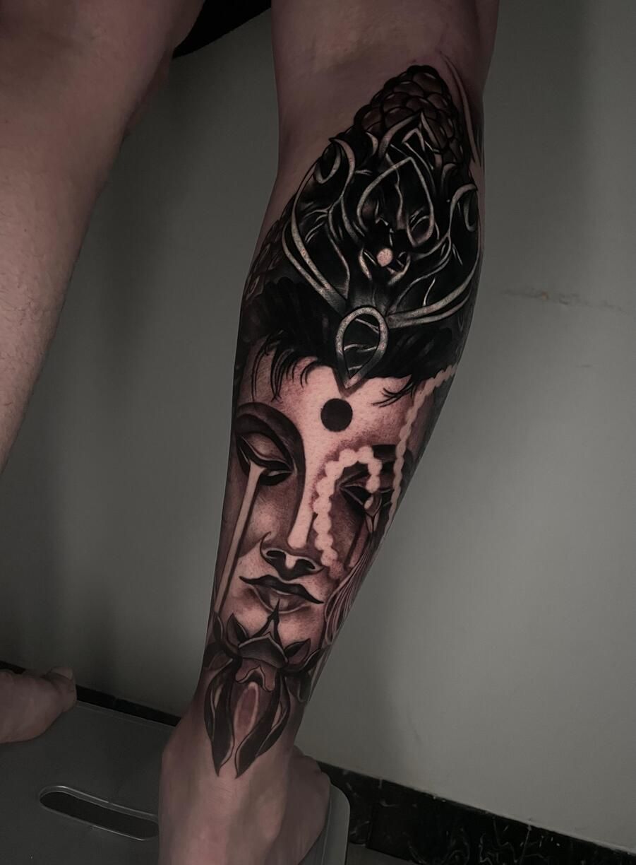 Tatuaje en una pierna que presenta un rostro de Buda detallado en blanco y negro con un tocado adornado.