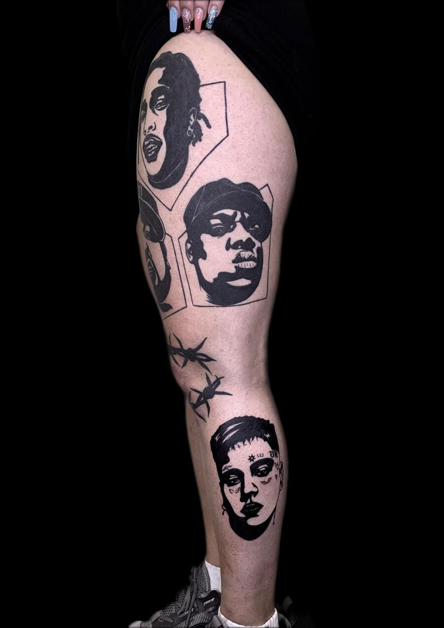 Pierna con tatuajes negros de caras, insectos y formas abstractas, sobre un fondo negro.